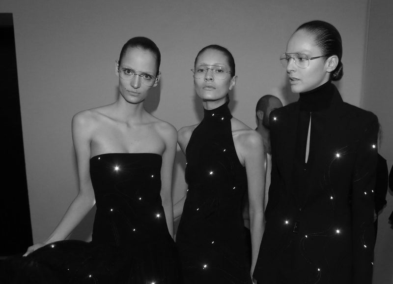 Three models in black evening wear backstage at the Akris fashion show in Paris.