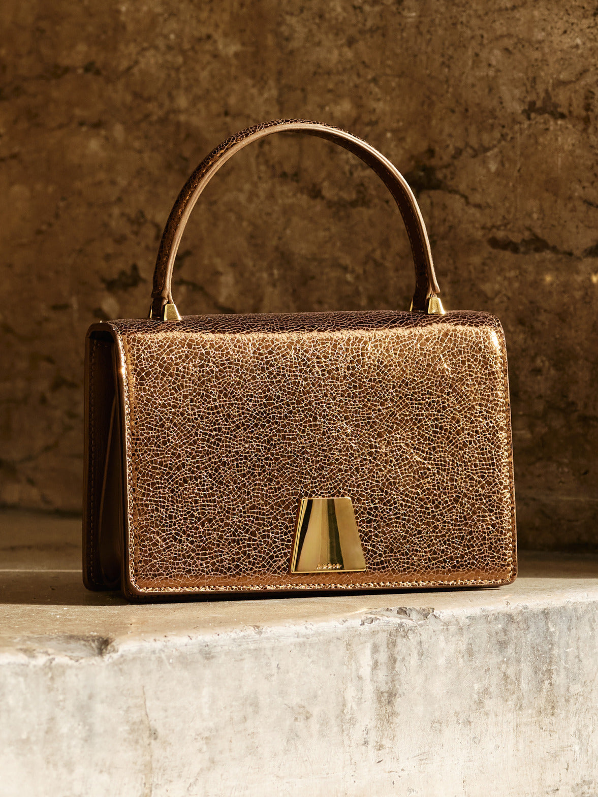 Akris Alice Top Handle Bag in metallic bronze leather, featuring a structured silhouette and signature trapezoid closure.
